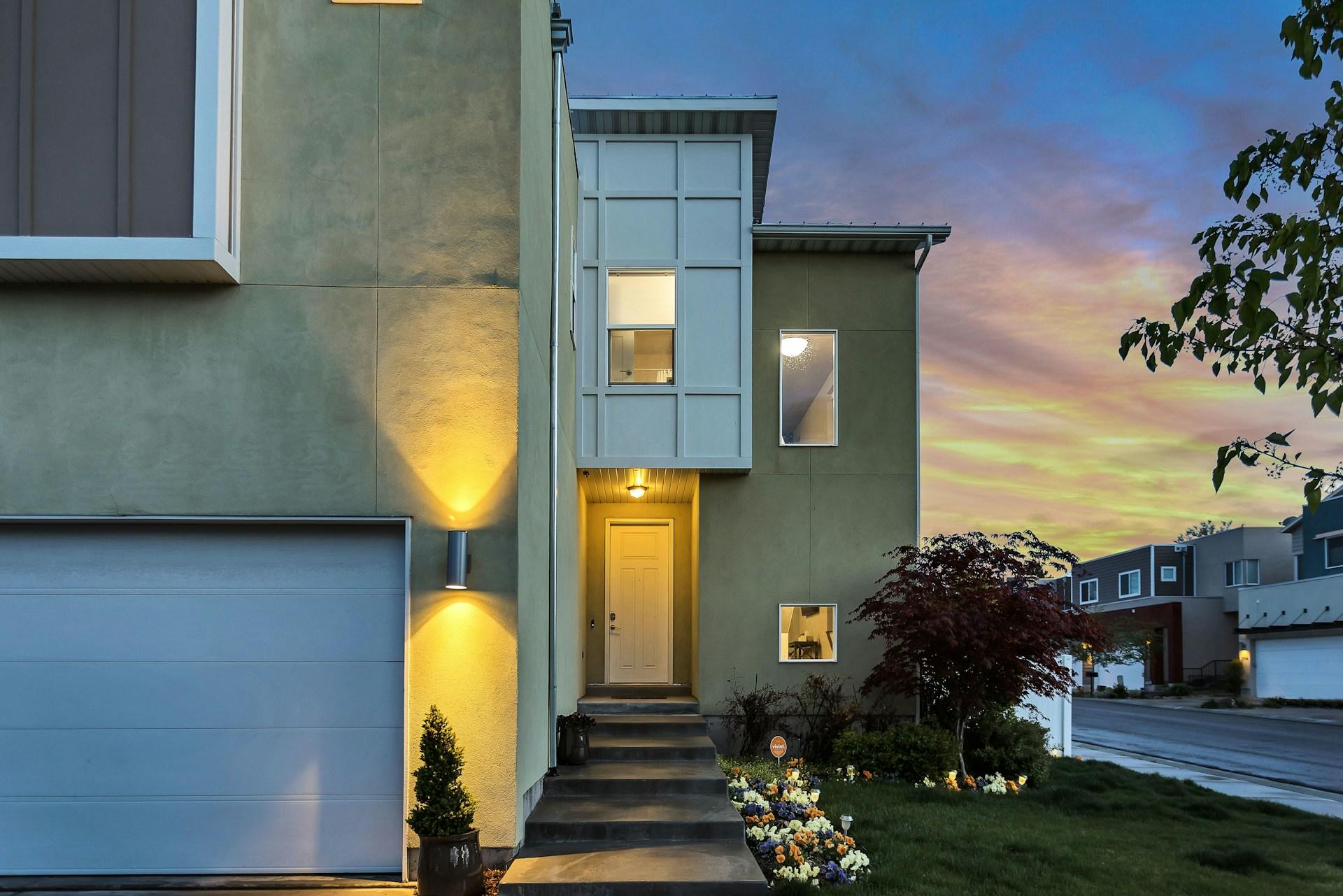 Modern house entrance at dusk with lights and flowers.